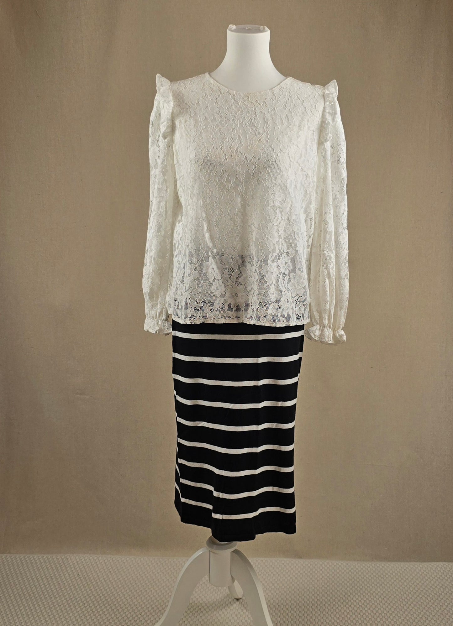 Weißes Spitzenshirt mit langen Ärmeln über einem schwarz-weiß gestreiften Rock – Vorderansicht auf Büste.