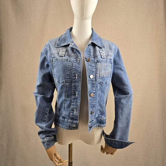 Vintage-Jeansjacke von Roccobarocco in Mittelblau mit silbernen Knöpfen und glitzerndem Logo-Schriftzug – Look der Woche bei Mediterrana