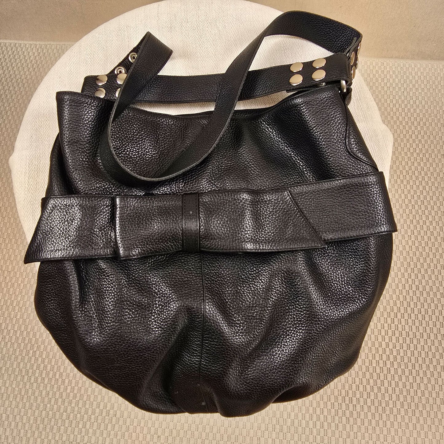 Schwarzer Ledershopper mit markanter Schleife und silbernen Nieten – edles Replikat im Stil von Armani, aus weichem, schwerem Leder, stilvoll inszeniert auf rundem, hellen Untergrund.
