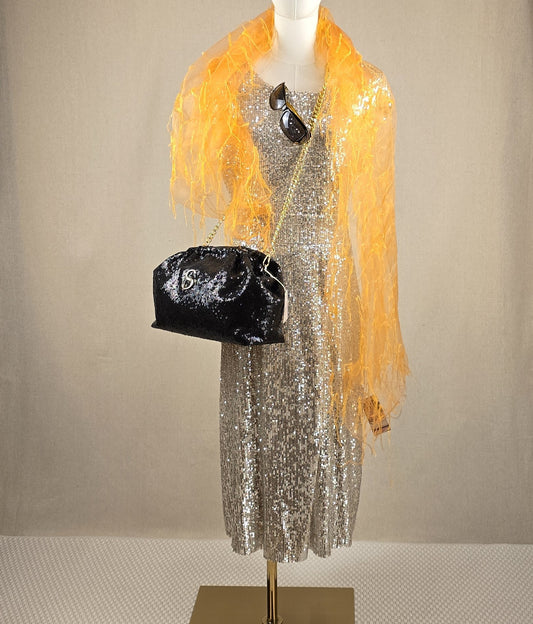 Goldenes Paillettenkleid auf Schneiderpuppe, kombiniert mit orangefarbenem Schal, Sonnenbrille und schwarzer Sorena-Tasche – Mediterrana Look der Woche