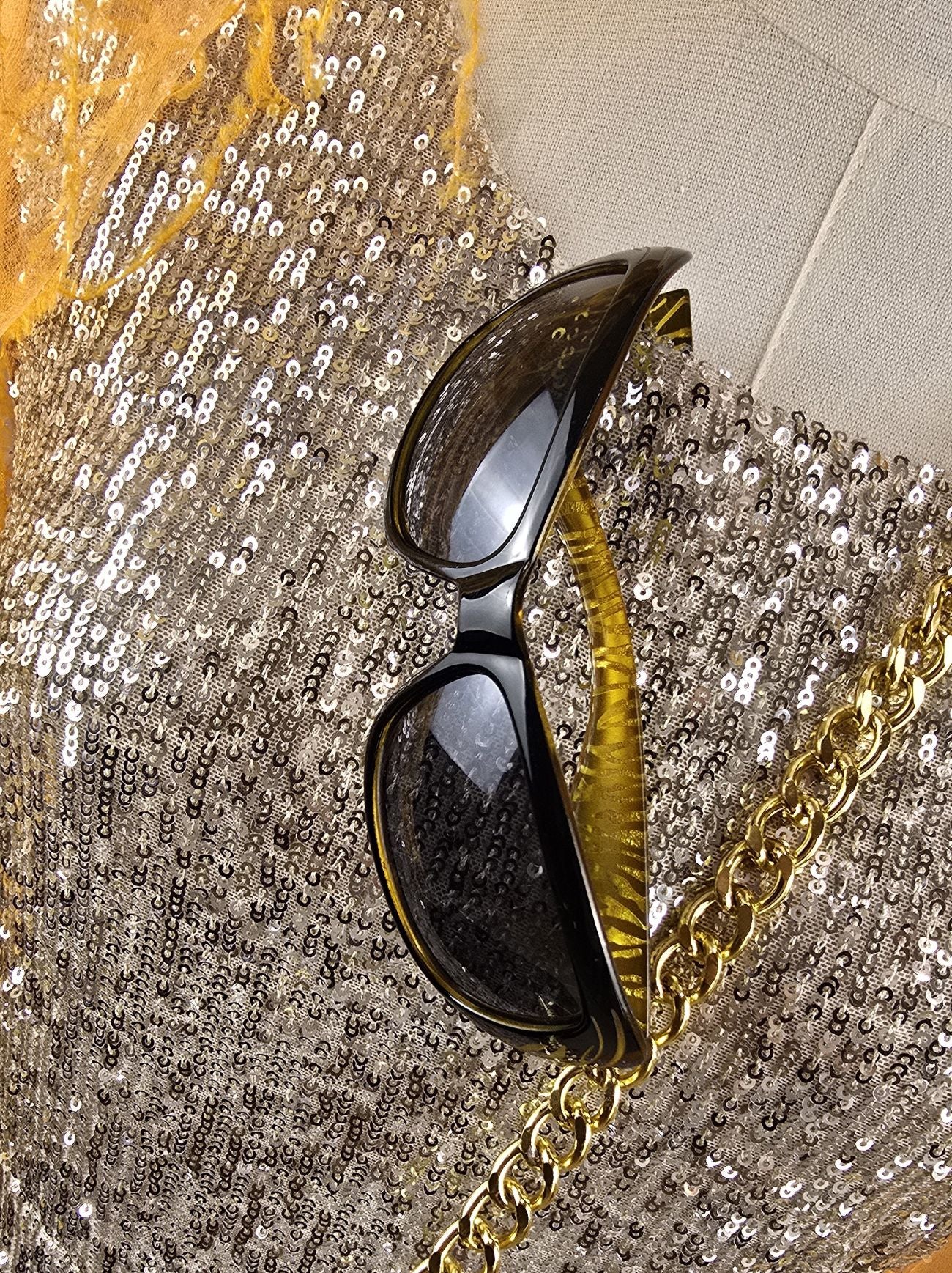 Sonnenbrille im Tigerlook auf goldenem Paillettenkleid – stilvoller Materialkontrast in der Detailansicht
