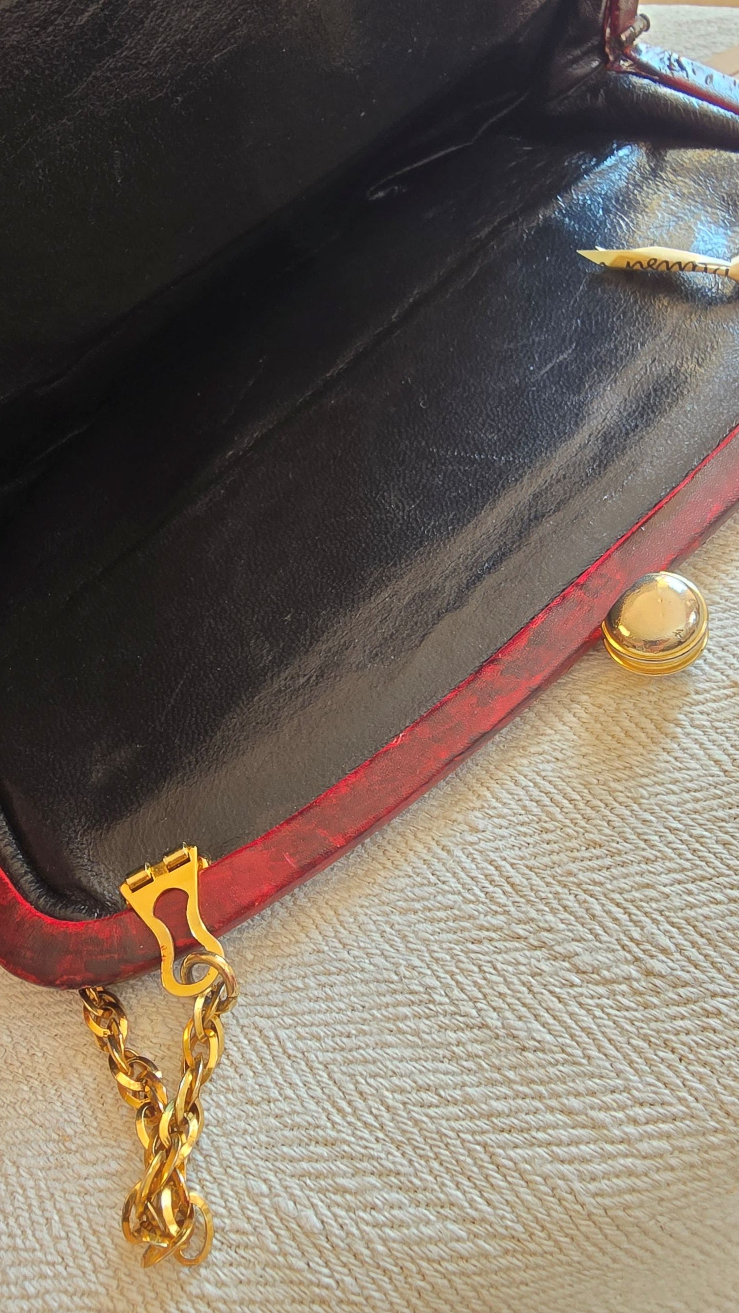 Innenansicht einer bordeauxfarbenen Vintage-Tasche – schwarzes Lederfutter, goldener Verschluss und Kettendetail sichtbar