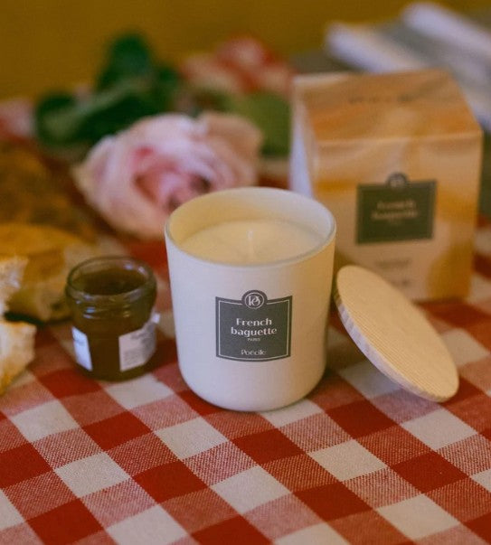 Poécile French Baguette Duftkerze 190 g auf rot-weiß kariertem Tisch mit Baguette, Croissant und Marmeladenglas