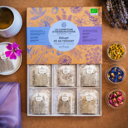 Bio-Teebox Träumen und Entspannen von Le Comptoir d’Herboristerie mit sechs Sorten und 30 Teebeuteln, arrangiert mit Tasse, Blüten und Kräutern.