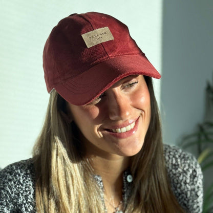 Model mit bordeauxroter De La Mur Bore Samtkappe mit gebogenem Schirm und beigefarbenem Markenlabel