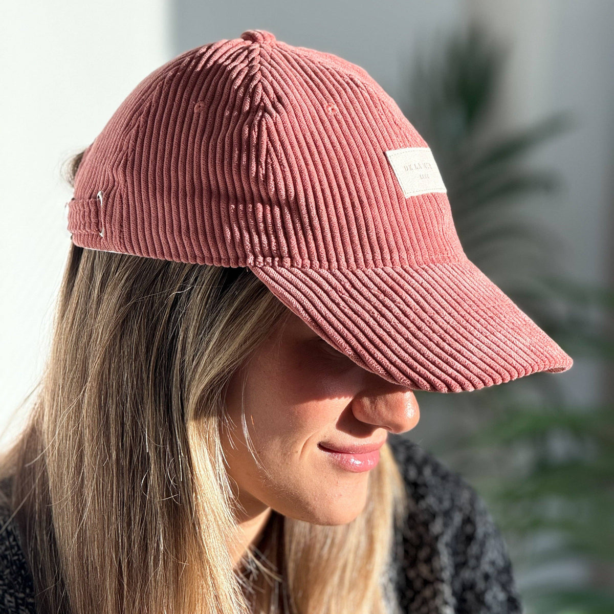 Model mit korallenfarbener De La Mur Coral Cordkappe mit gebogenem Schirm und camelfarbenem Markenlabel