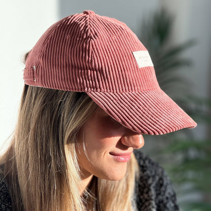 Model mit korallenfarbener De La Mur Coral Cordkappe mit gebogenem Schirm und camelfarbenem Markenlabel