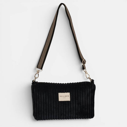 Schwarze De La Mur Curly Clutch aus breitem Cord mit schwarz-beigem Schultergurt auf hellem Hintergrund.