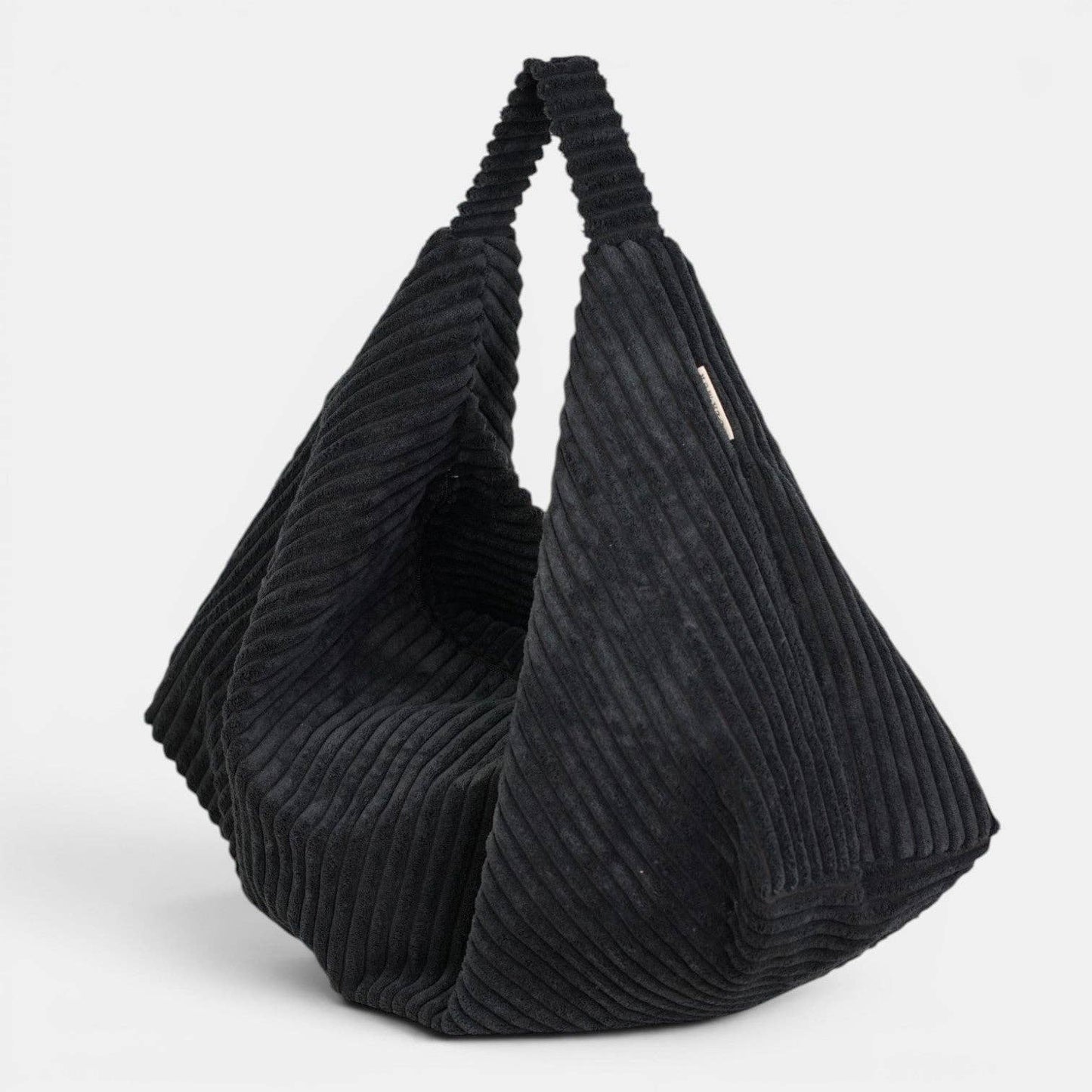 Schwarze De La Mur Curly Cookie Schultertasche aus breitem Cord in gefalteter Glückskeksform auf hellem Hintergrund.