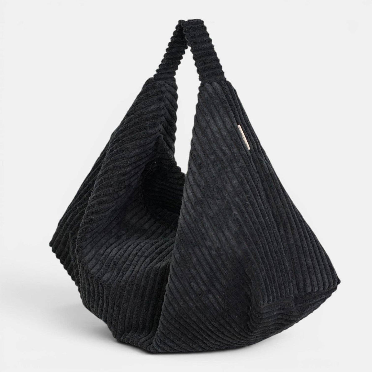 Schwarze De La Mur Curly Cookie Schultertasche aus breitem Cord in gefalteter Glückskeksform auf hellem Hintergrund.