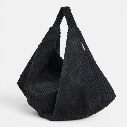 Schwarze De La Mur Curly Cookie Schultertasche aus breitem Cord in gefalteter Glückskeksform auf hellem Hintergrund.