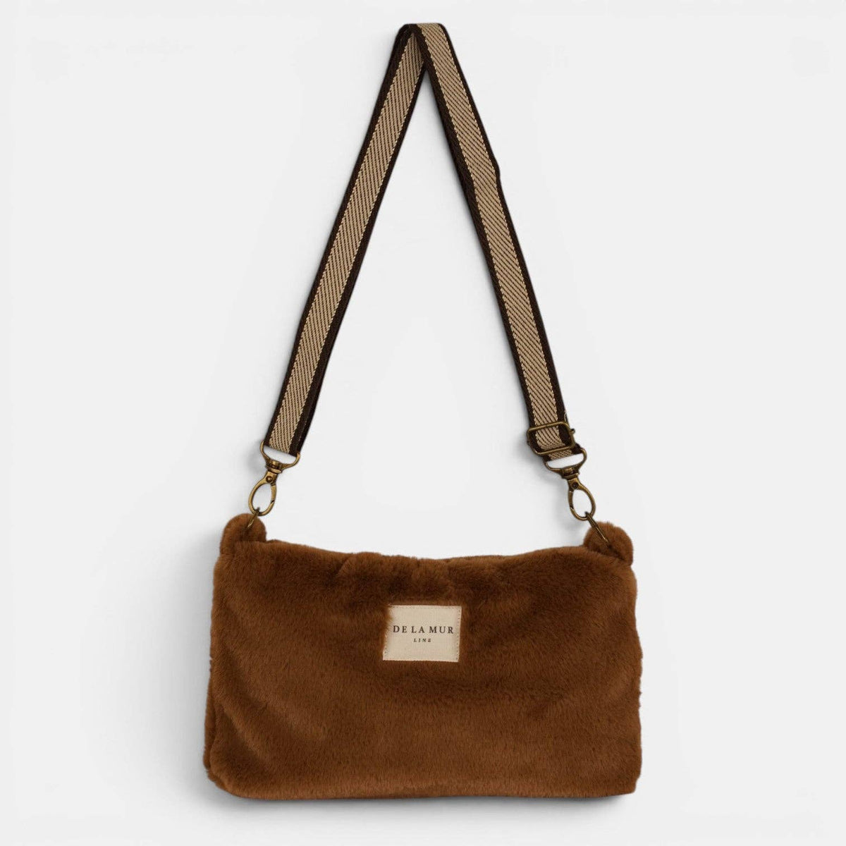 Braune De La Mur Pile Clutch mit flauschiger Felloptik und beigefarbenem Tragegurt auf hellem Hintergrund.