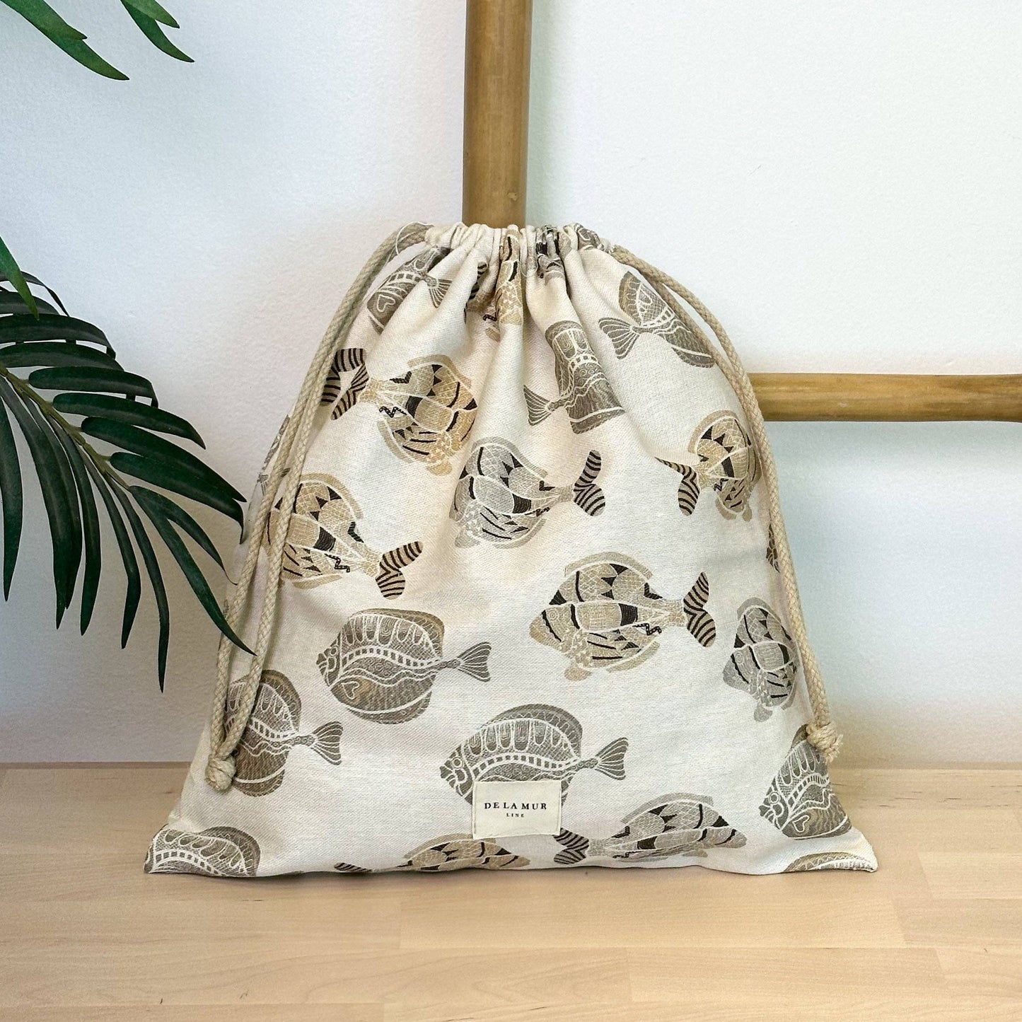 Snackbeutel Taba von De La Mur mit Fischmotiv in Beige-, Grau- und Brauntönen, dekoriert auf einem Holztisch.Snackbeutel Taba von De La Mur mit Fischmotiv in Beige-, Grau- und Brauntönen, dekoriert auf einem Holztisch.