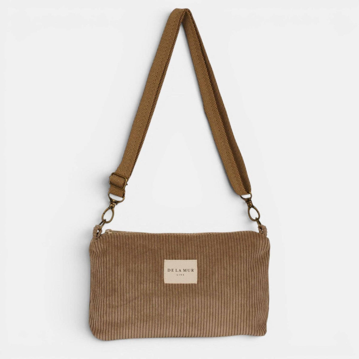 Beige De La Mur Toast Clutch aus breitem Cord mit verstellbarem Tragegurt auf hellem Hintergrund.