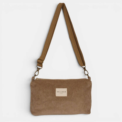 Beige De La Mur Toast Clutch aus breitem Cord mit verstellbarem Tragegurt auf hellem Hintergrund.