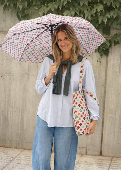 Model mit geöffnetem De La Mur Zag Taschenschirm mit mehrfarbigem geometrischem Muster auf naturfarbenem Grund