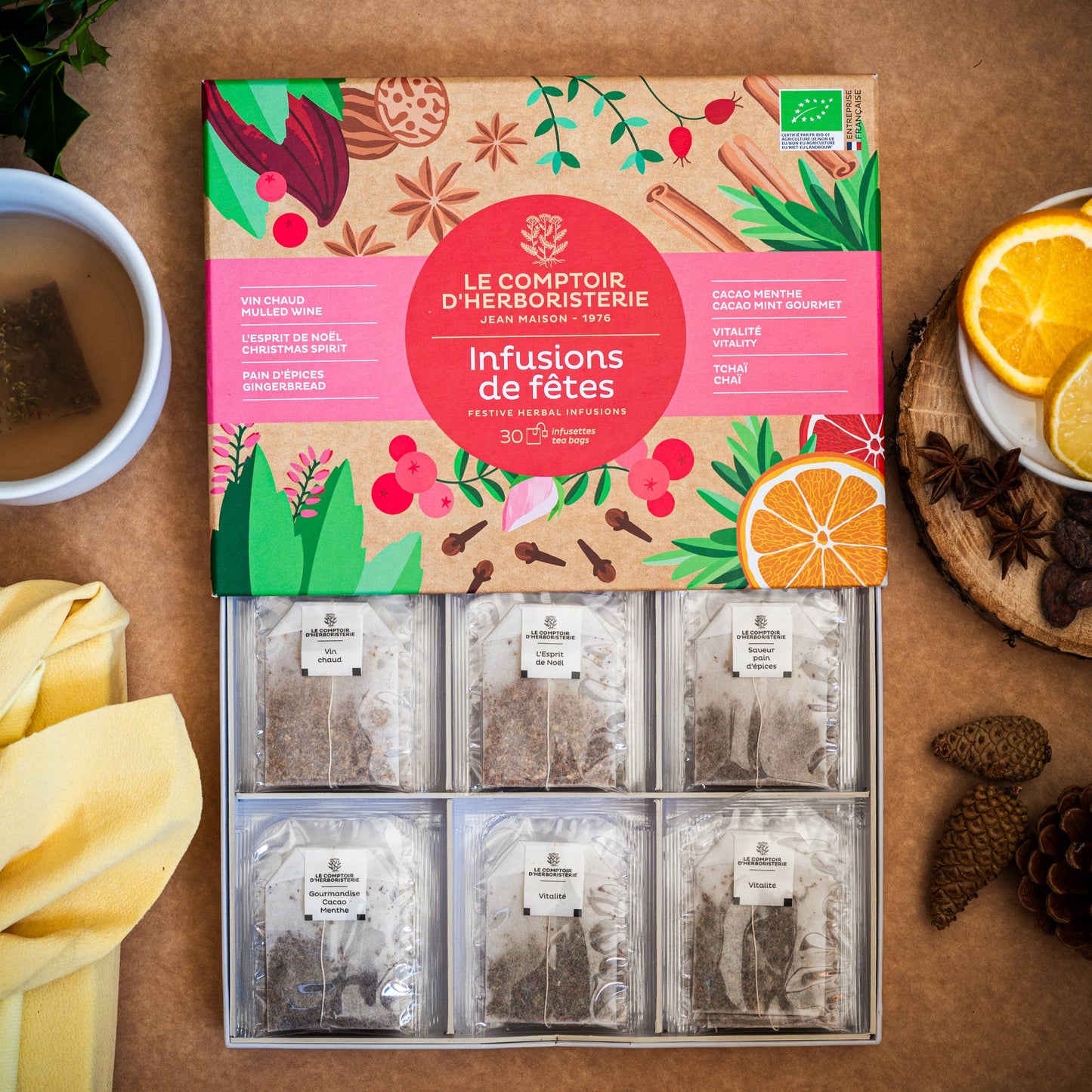 Festliche Bio-Tee-Geschenkbox von Le Comptoir d’Herboristerie mit sechs Sorten und 30 Teebeuteln, arrangiert mit Tasse, Orangen und winterlichen Gewürzen.