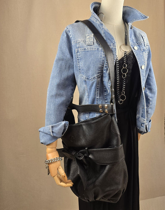 Komplettlook mit schwarzem CrAnna-Kleid, Vintage-Jeansjacke, schwarzem Ledershopper im Armani-Stil, Statementkette und Boots – fotografiert auf rundem Tisch mit sanftem Licht.